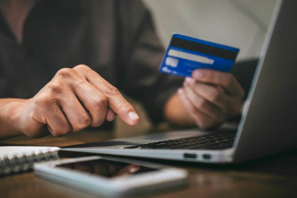 Person am Laptop während eines Zahlvorgangs mit Kreditkarte in der Hand